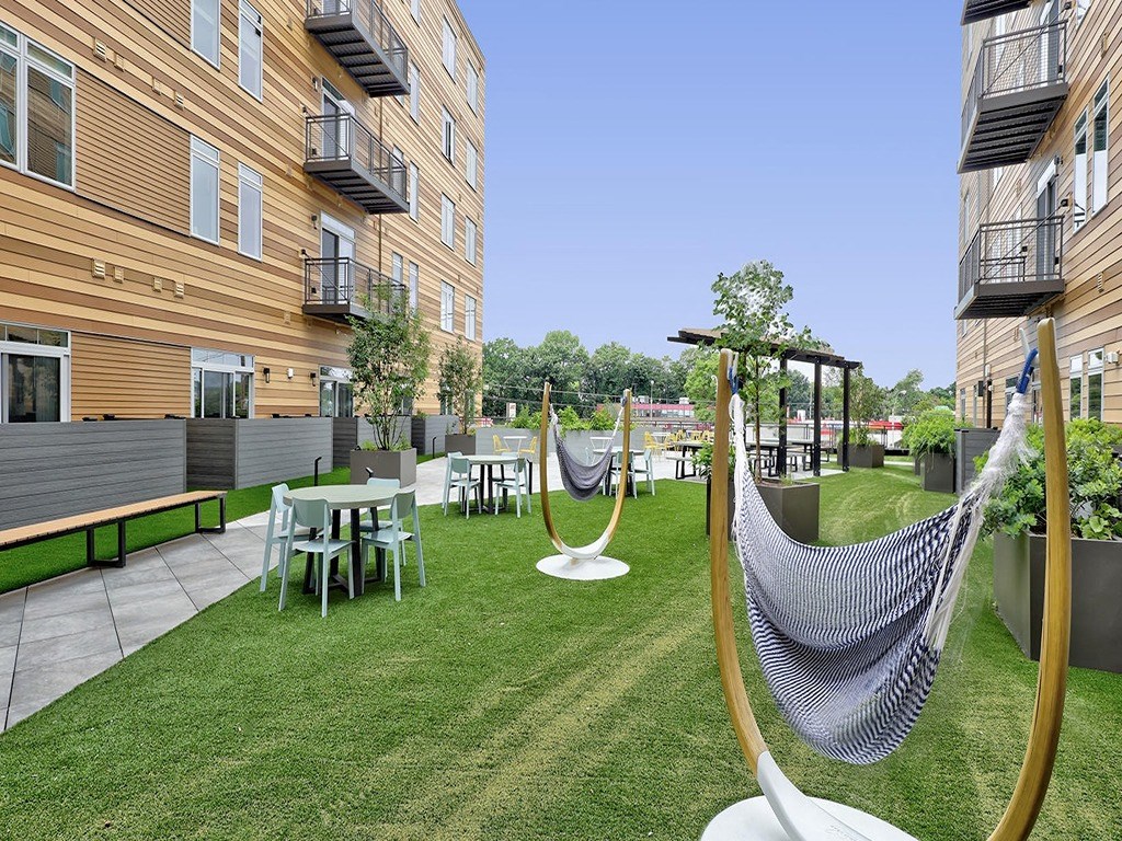 a yard with hammocks and tables and chairs in an apartment building